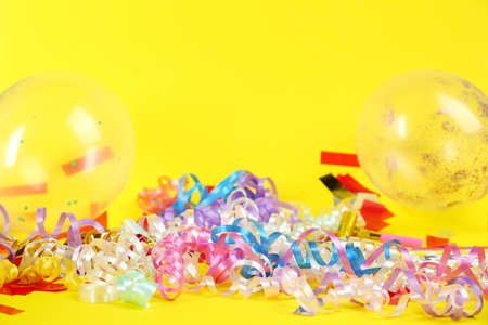 Colorful serpentine streamers, confetti and balloons on yellow background, space for textの写真素材