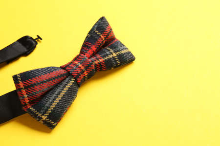 Stylish tartan bow tie on yellow background, closeup. Space for text