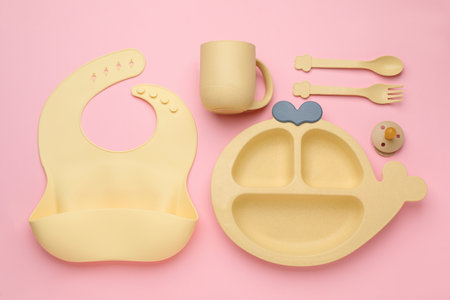 Flat lay composition with baby feeding accessories and bib on pink background