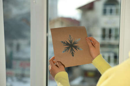 Woman holding snowflake stencil near window at home, closeup