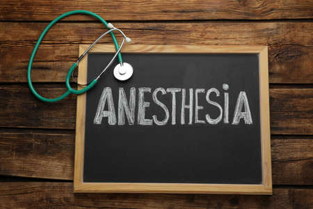 Blackboard with word Anesthesia and stethoscope on wooden table, top viewの写真素材