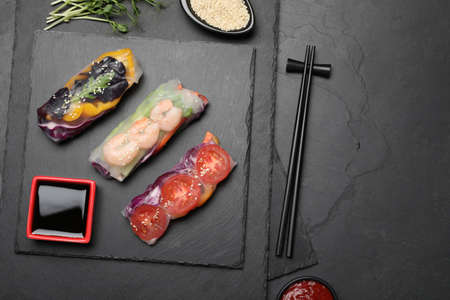 Delicious rolls wrapped in rice paper served on black table, flat lay. Space for text