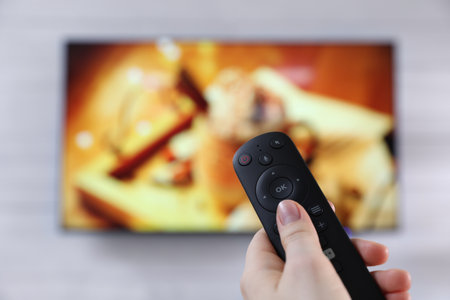 Woman with remote control watching TV at home, closeup. Space for textの写真素材