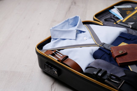 Packed suitcase with business trip stuff on wooden surface. Space for textの写真素材
