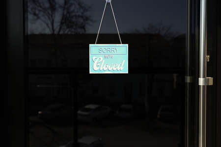 Light blue sign with text Sorry we're Closed hanging on glass door. Coronavirus quarantine
