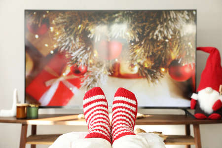Woman in cute knitted socks watching TV at home, closeupの写真素材