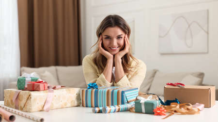 Young woman with beautifully wrapped gifts at table in living roomの写真素材