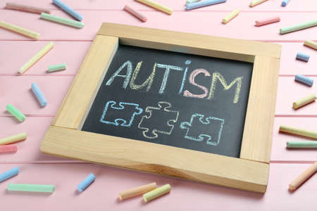Blackboard with word Autism and drawn jigsaw puzzle pieces surrounded by colorful chalks on pink wooden backgroundの写真素材