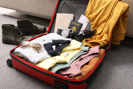 Open suitcase with clothes, accessories and shoes on floor indoors, closeup
