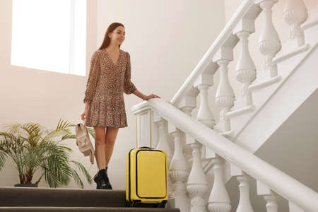 Happy young woman with suitcase on stairs in hotelの写真素材