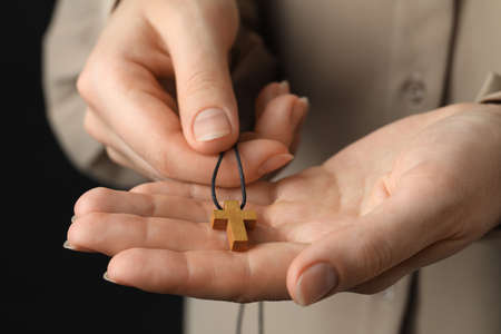 Woman holding wooden Christian cross on black background, closeupの写真素材