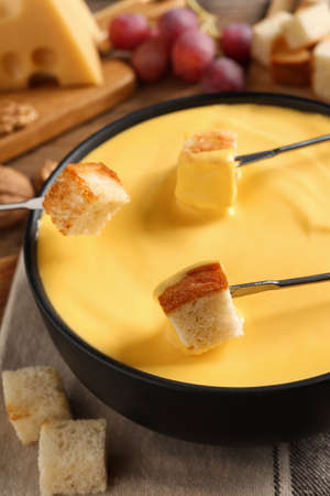 Dipping pieces of bread into tasty cheese fondue at table, closeupの写真素材