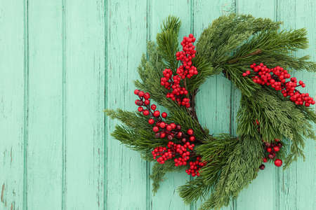 Beautiful Christmas wreath with red berries hanging on turquoise wooden wall, space for textの写真素材