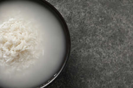Bowl with rice soaked in water on gray table, top view. Space for textの写真素材