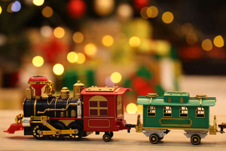 Beautiful toy train on wooden table against blurred festive lights. christmas celebration
