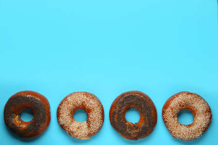 Many delicious fresh bagels on light blue background, flat lay. Space for text