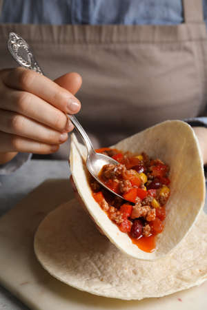 Woman putting tasty chili con carne into tortilla at white table, closeupの写真素材