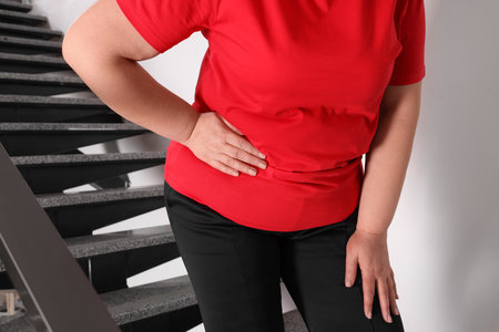 Overweight mature woman suffering from pain in right side on stairs indoors, closeupの写真素材