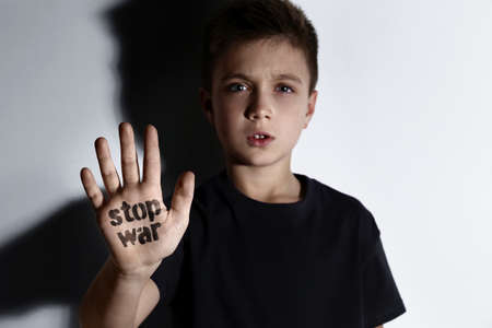 Unhappy little boy showing palm with phrase Stop War near white wallの写真素材
