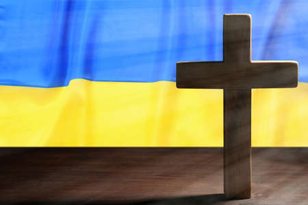 Pray for Ukraine. Cross on wooden table against Ukrainian flag, space for textの写真素材