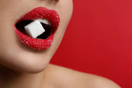 Woman with beautiful lips eating sugar cube on red background, closeup. Space for textの写真素材