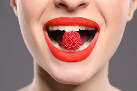 Young woman with beautiful red lips makeup eating candy on gray background, closeupの写真素材