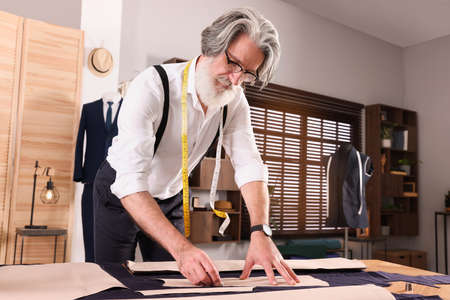 Professional tailor marking sewing pattern on fabric with chalk at table in workshopの写真素材