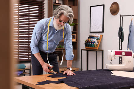 Professional tailor cutting fabric by following chalked sewing pattern at table in workshop