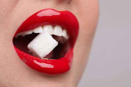 Closeup view of young woman with beautiful lips eating sugar cube on light gray backgroundの写真素材
