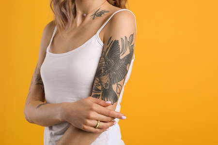 Beautiful woman with tattoos on body against yellow background, closeup. Space for textの写真素材