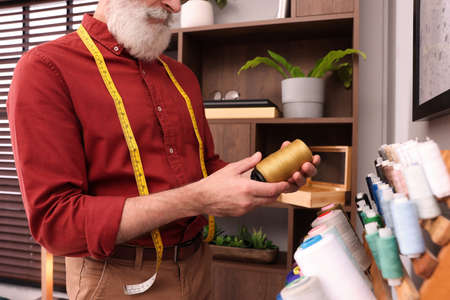 Professional tailor choosing thread near stand in workshop, closeup