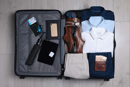 Folded clothes, shoes and accessories in open suitcase on wooden background, top view. Packing for business tripの写真素材