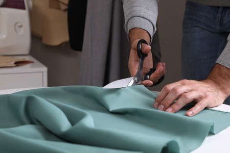 Tailor cutting fabric with scissors at table in atelier, closeupの写真素材