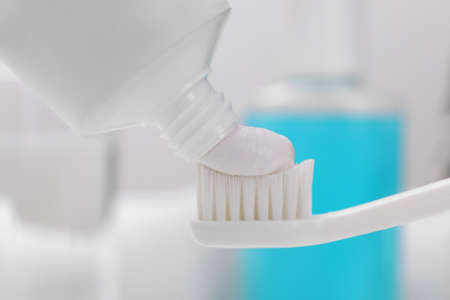 Squeezing paste onto toothbrush against blurred background, closeup
