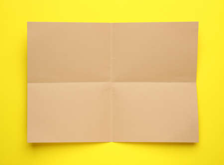Sheet of brown paper on yellow background, top view