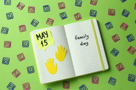 happy family day. Notebook with text and decorative paper clips on light green background, flat lay