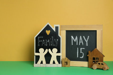 Happy International Family Day. Small chalkboards with text, house models, people figures and toy car on green table against yellow backgroundの写真素材