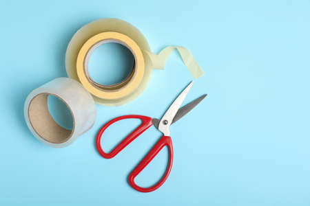 Rolls of adhesive tape and scissors on light blue background, flat lay. Space for textの写真素材