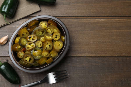 Fresh and pickled green jalapeno peppers on wooden table, flat lay. Space for textの写真素材