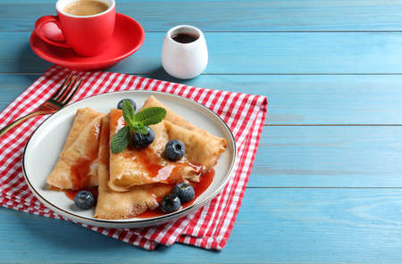 Delicious crepes served with blueberries, mint, syrup and cup of coffee on blue wooden table. Space for textの写真素材