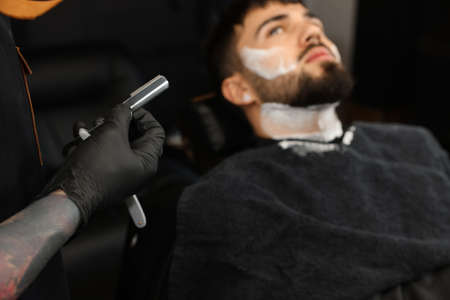 Professional hairdresser working with bearded client in barbershop, closeupの写真素材