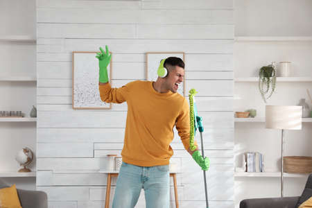 Man in headphones with mop singing while cleaning at home