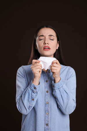 Sick young woman sneezing in tissue on dark background. cold symptomsの写真素材