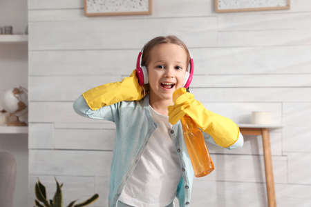 Cute little girl in headphones with bottle singing while cleaning at homeの写真素材