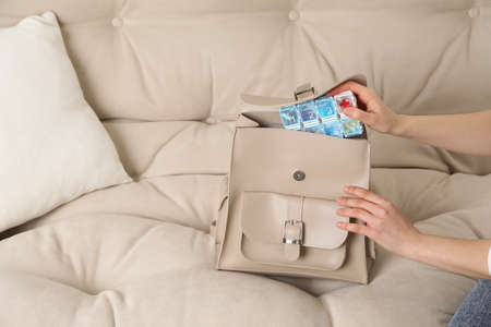 Woman putting pill box into backpack on sofa, closeup