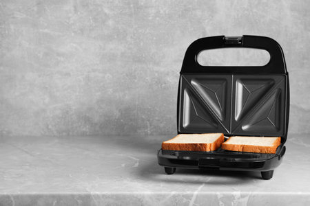 Modern sandwich maker with bread slices on gray table, space for textの写真素材