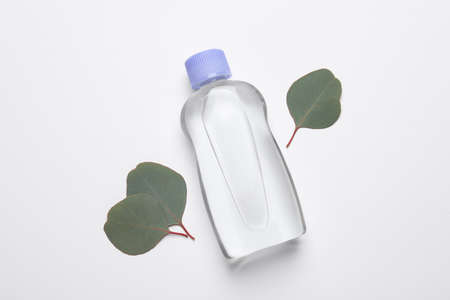 Bottle of baby oil and eucalyptus leaves on white background, flat lay