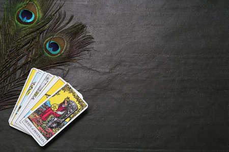 Tarot cards and peacock feathers on black table, flat lay. Space for textの写真素材