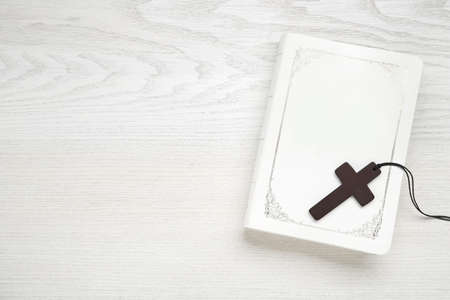 Wooden Christian cross and Bible on white table, top view. Space for textの写真素材