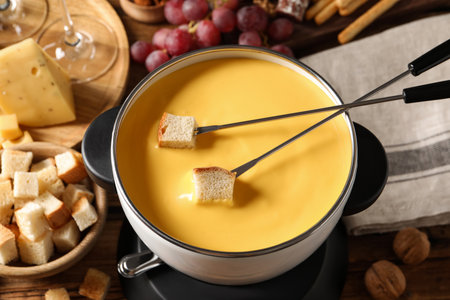 Pot of tasty cheese fondue, forks with bread pieces and snacks on table, above viewの写真素材